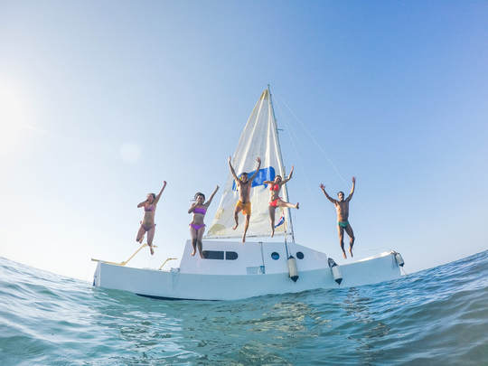 Happy friends jumping off the catamaran boat into the ocean